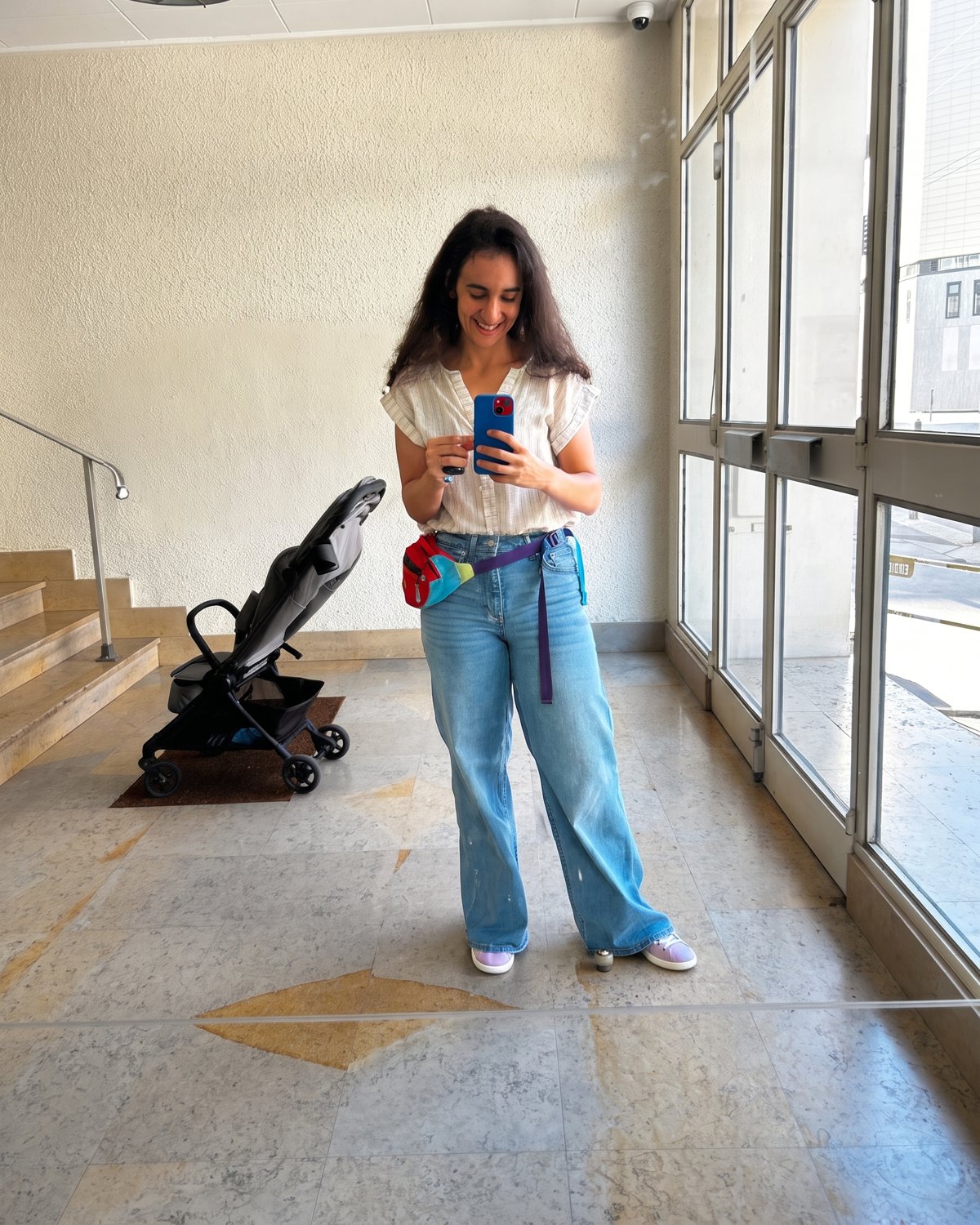 Laila today, smiling, phone in hand, the stroller behind her